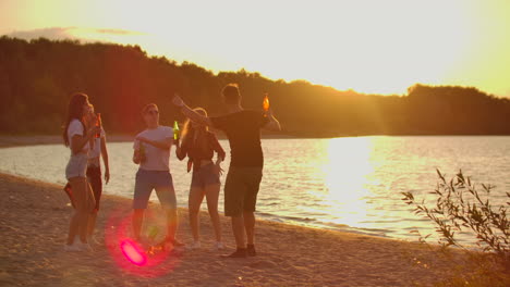 The-five-students-celebrate-end-of-educational-year-on-the-open-air-party-on-the-lake-coast-with-beer.-It-is-crazy-and-hot-beach-party-between-the-best-friends-around-bonfire.